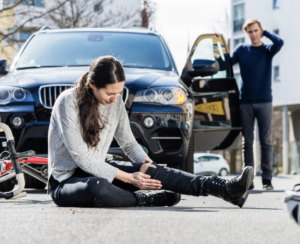 A woman in a gray sweater sits on the road clutching her knee after a bicycle accident